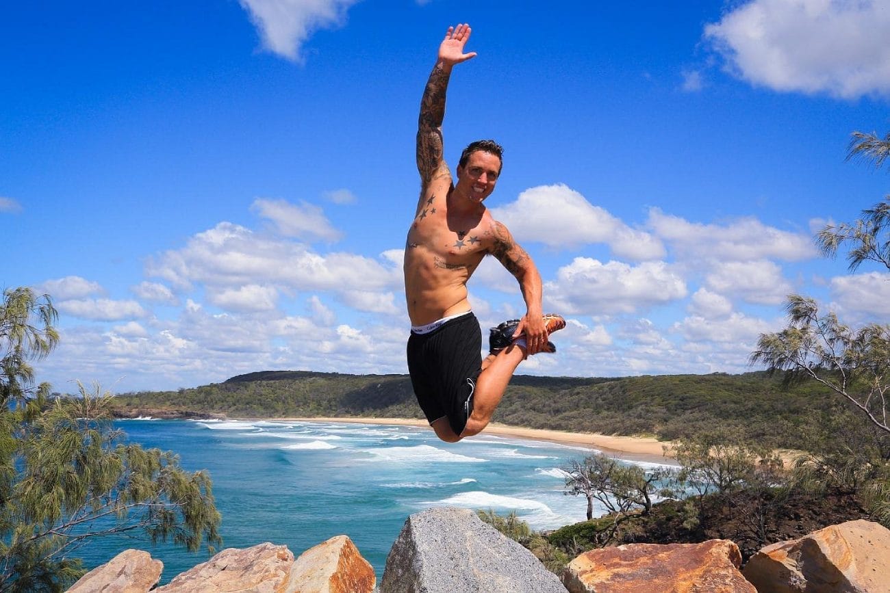 Man jumping on coastal rocks at Noosa National Park with ocean behind him  photo by John Hallam