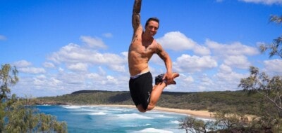 Man jumping on coastal rocks at Noosa National Park with ocean behind him – photo by John Hallam